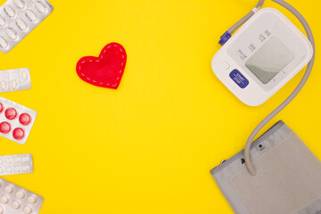 The concept of health, cardiology, blood pressure. Blood pressure monitor, pills and tissue heart on a yellow background. Top view, free space for text.