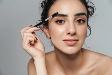 Fotobehang Image of half-naked woman using cosmetic brush for her eyebrows © Drobot Dean