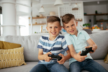 Happy brothers playing video games. Young brothers having fun while playing video games in living room.