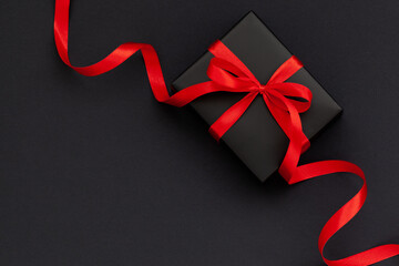 Black Friday concept. Top view of black gift box with red ribbon on black and red background with...