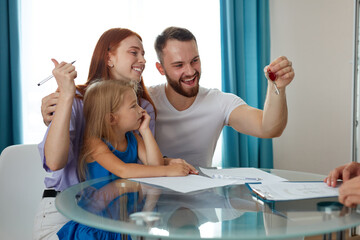 happy male with wife and daughter get keys from their first house, they sit excited, sign the documents to get mortgage