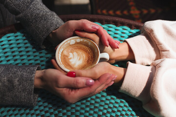 Mature mother and her young daughter sit together in cafe or restaurant. Up view of female hands holding one cup of coffee together. Love and support. Family connection.