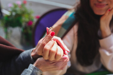 Mature mother and her young daughter sit together in cafe or restaurant. Cut view of girl holding engagement ring with fingers and rejoice. Mother support share her happiness. Getting married soon.