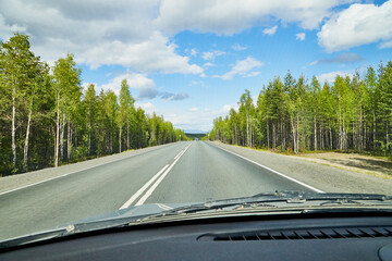 View from car window on the road and landscape with forest, tees, and blue sky with clouds. Landscape through windscreen with a relief