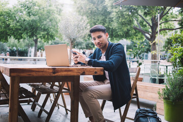 Smiling young man using laptop in street cafe