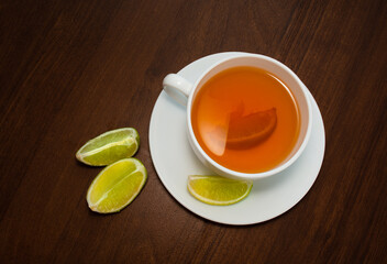  cup of black tea on a saucer with lime slices on a dark brown wooden background