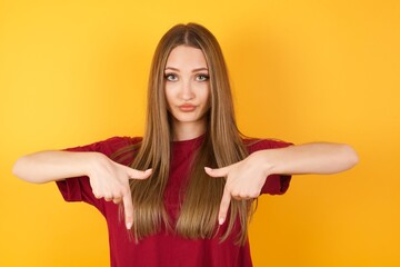 Beautiful Young beautiful caucasian girl wearing red t-shirt over isolated yellow background pointing with two fingers at copy space down. Place for advertising