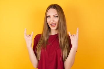Beautiful Young beautiful caucasian girl wearing red t-shirt over isolated yellow background posing in studio. showing rock and roll hand gesture
