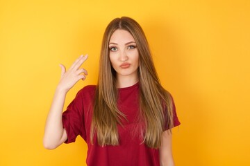 Unhappy Beautiful Young beautiful caucasian girl wearing red t-shirt over isolated yellow background imitates gun shoot makes suicide gesture keeps two fingers on temples has puzzled expression