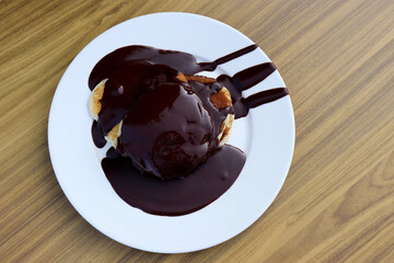 Pancakes drizzled with chocolate sauce in a white plate on wooden table, top view. Tasty dessert, sweet breakfast