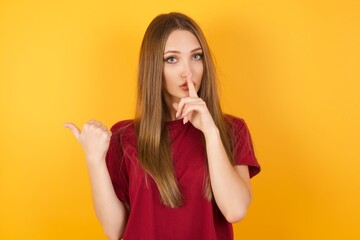 Beautiful Young beautiful caucasian girl wearing red t-shirt over isolated yellow background asking to be quiet with finger on lips pointing with hand to the side. Silence and secret concept.