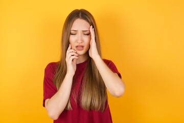 Doleful desperate crying Beautiful Young beautiful caucasian girl wearing red t-shirt over isolated yellow background being in depression  looks stressfully, frowns face, 