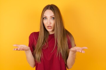 Frustrated caucasian male isolated over yellow background. feels puzzled and hesitant, shrugs shoulders in bewilderment, keeps mouth widely opened, doesn't know what to do.