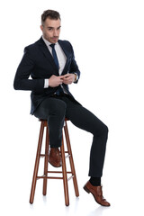 Confident businessman fixing his jacket while sitting on a stool