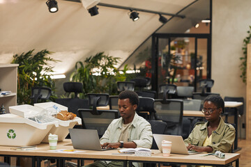 Portrait of two African-American people using laptop while working by waste sorting bins in modern office, copy space