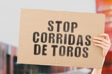The phrase " Stop corridas de toros " in Spanish language on a banner in men's hand with blurred background. Equality. Violence. Animal rights. Illegal. Fights. Pain