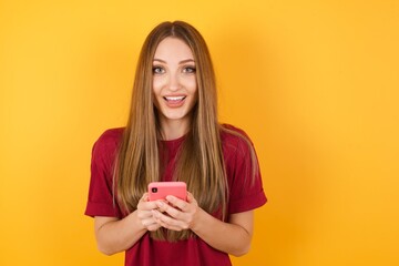 Copyspace photo of Beautiful Young beautiful caucasian girl wearing red t-shirt over isolated yellow background holding phone in his hands while