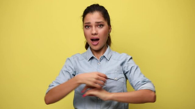 shocked young girl in blue jeans shirt crossing arms, opening mouth, showing muscles and pointing fingers to herself on yellow background 