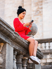 An attractive young female looking at her smartphone while sitting on a stone balusters