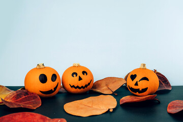 Little pumpkins with painted faces for Halloween with Autumn leaves on blue and black background