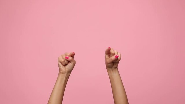 woman holding hands in the air, pointing fingers and dancing on pink background