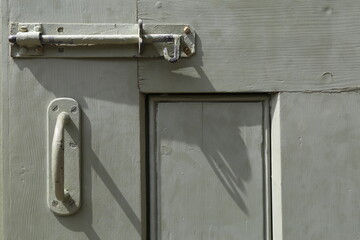 A closeup view of a door handle and tower bolt on an old, grey, wooden door.