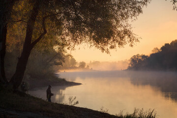 Men fishing in river with fly rod during summer morning. Beautiful fog.