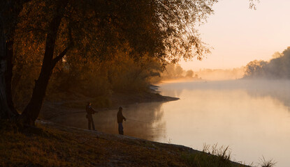 Men fishing in river with fly rod during summer morning. Beautiful fog.