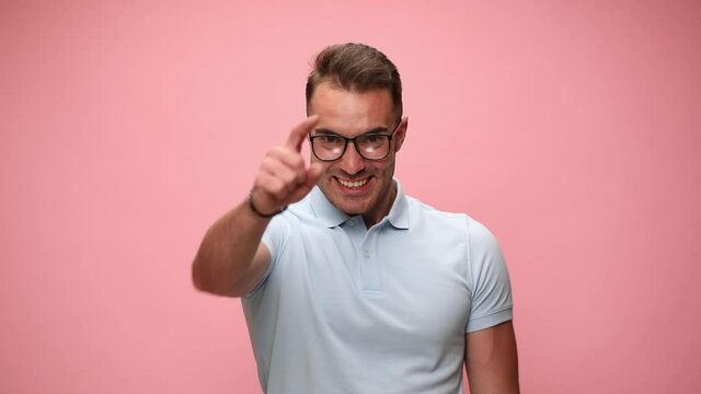 sexy casual man smiling wide, pointing at the camera, raising his trophy and celebrating succes on pink background