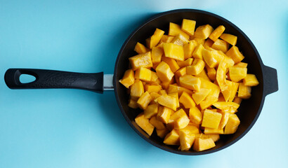 pieces of pumpkin in a black cast-iron pan, on a blue background. Seasonal vegetables, rich harvest, pumpkin sliced in a skillet. Diet, proper nutrition, healthy vegetables, vitamins all year round