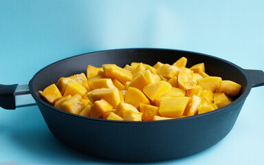 pieces of pumpkin in a black cast-iron pan, on a blue background. Seasonal vegetables, rich harvest, pumpkin sliced in a skillet. Diet, proper nutrition, healthy vegetables, vitamins all year round