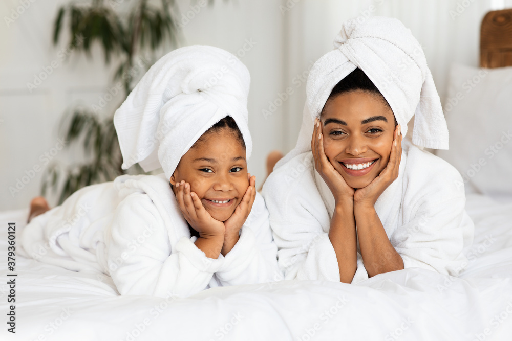 Wall mural happy black mom and daughter in bathrobes and towels posing on bed