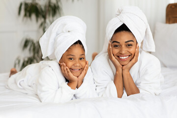 Happy Black Mom And Daughter In Bathrobes And Towels Posing On Bed