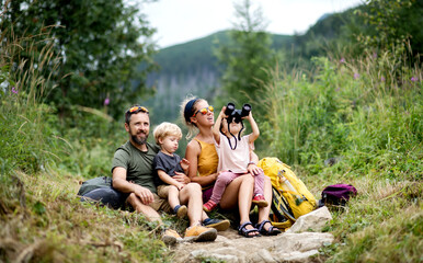 Family with small children hiking outdoors in summer nature, sitting and resting. - obrazy, fototapety, plakaty