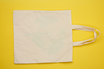 empty beige textile bag on yellow background, rejection of plastic bags, flat lay