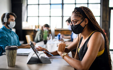 Business people with face masks indoors in office, back to work after coronavirus lockdown.