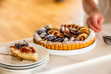 A woman cutting a colorful fig tart with icing sugar in the kitchen