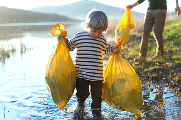 Father with small son collecting rubbish outdoors in nature, plogging concept.