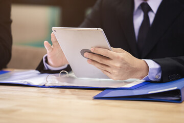 Close up hand businessman using digital tablet and writing data on paper work in office.