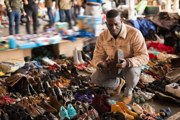 Afro-American guy considers sacond hands shoes on flea market