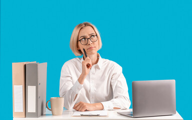 Attractive businesswoman lost in thought at workplace near laptop computer, blue studio background