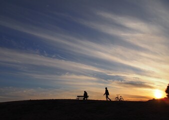 Fototapeta na wymiar 夕焼けを見るためにベンチに座っている人と自転車で駆けつけた人のシルエット