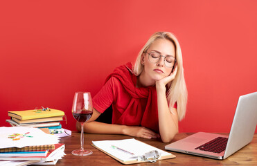 sleepy blonde puzzled caucasian woman employee in office sit work at desk, she has no energy to work, isolated red background