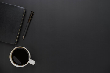 Top view above of dark black office desk table with notebook and coffee cup with a pen. Business...