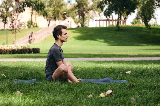 Young man in sportswear doing yoga in the park. Practice asana outdoors. Exercising on green grass on yoga mat. Man sitting in butterfly lotus pose, calm and meditation.Fitness and healthy lifestyle