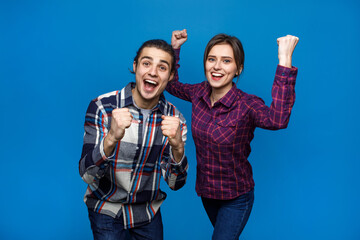 Beautiful young couple over blue background very happy and excited doing winner gesture with arms raised, smiling and screaming for success