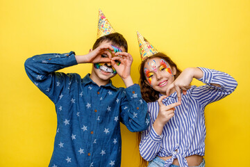 Beautiful children in party cap on yellow background, posing with love