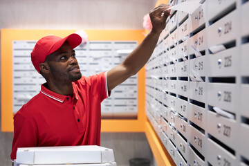 young african courier puts order in the mailbox in the entrance, enjoy working in delivery company