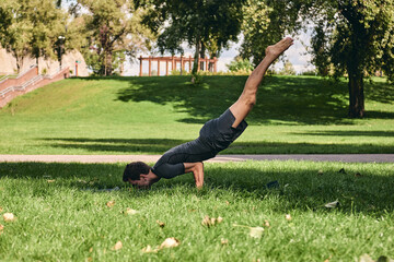 Young athletic man in sportswear doing yoga in the park. Practice asana outdoors. People exercising on green grass with yoga mat. Strong mature caucasian man in difficult peacock pose