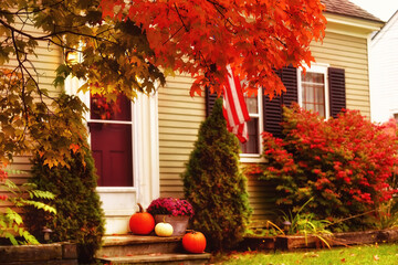 Pumpkins and autumn flowers on the porch of the house. Bright leaves of a red maple tree near the...